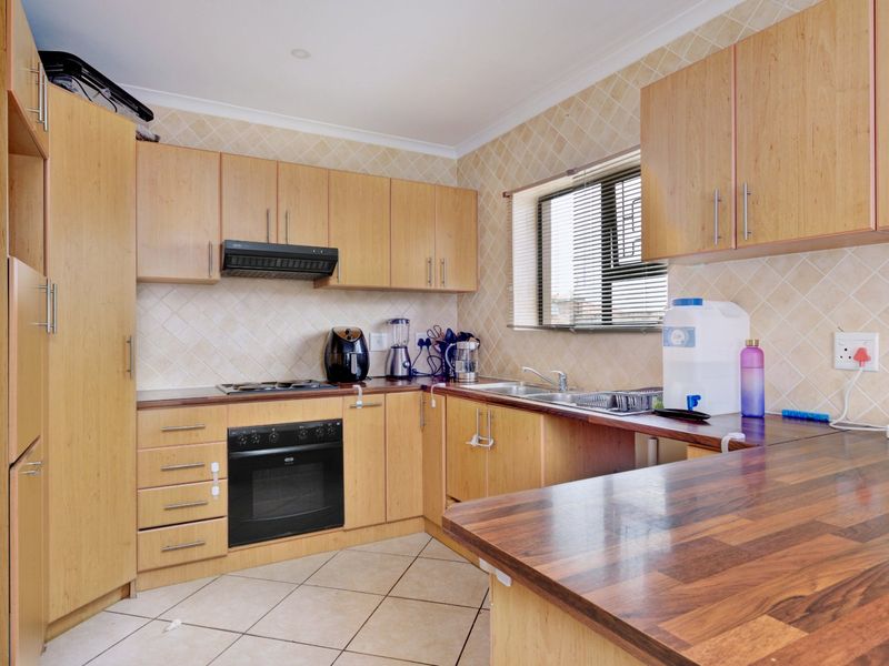 A functional kitchen featuring light wood cabinetry, dark laminate countertops, built-in oven, hob, extractor fan, and tiled finishes throughout.