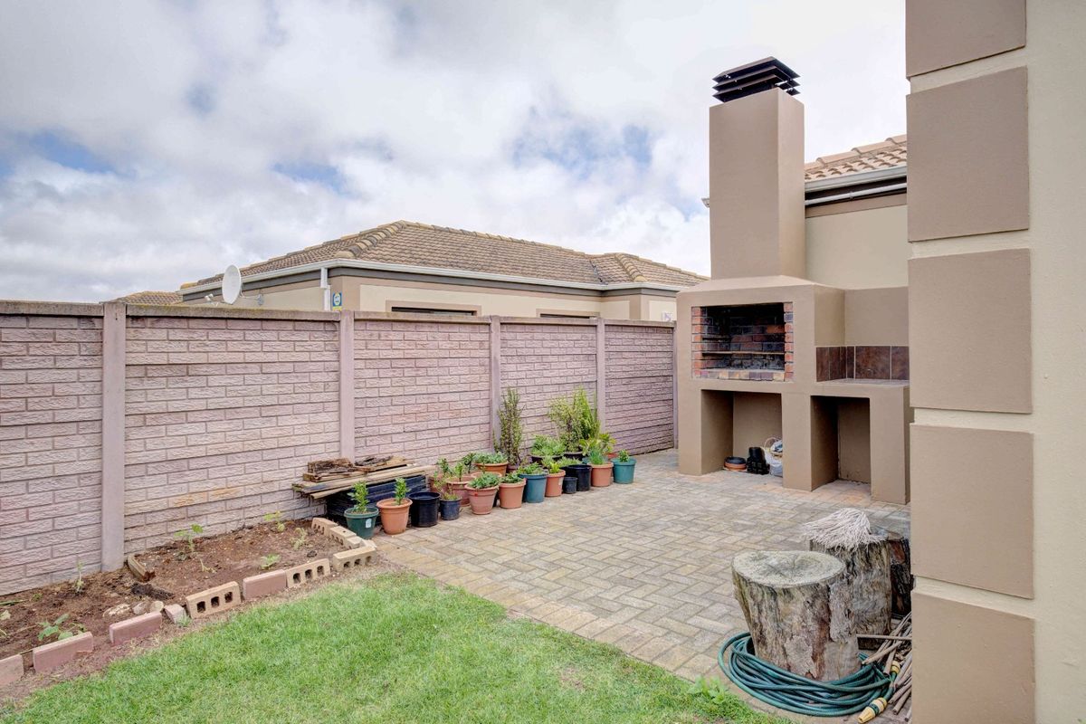 Rear courtyard featuring a built-in braai, brick paved patio area, and a secure precast boundary wall.