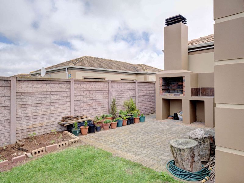 Rear courtyard featuring a built-in braai, brick paved patio area, and a secure precast boundary wall.