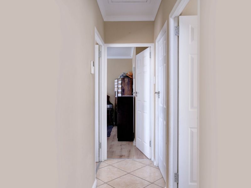 A clean, neutral-toned hallway featuring tiled flooring and multiple panelled interior doors providing access to adjacent rooms.