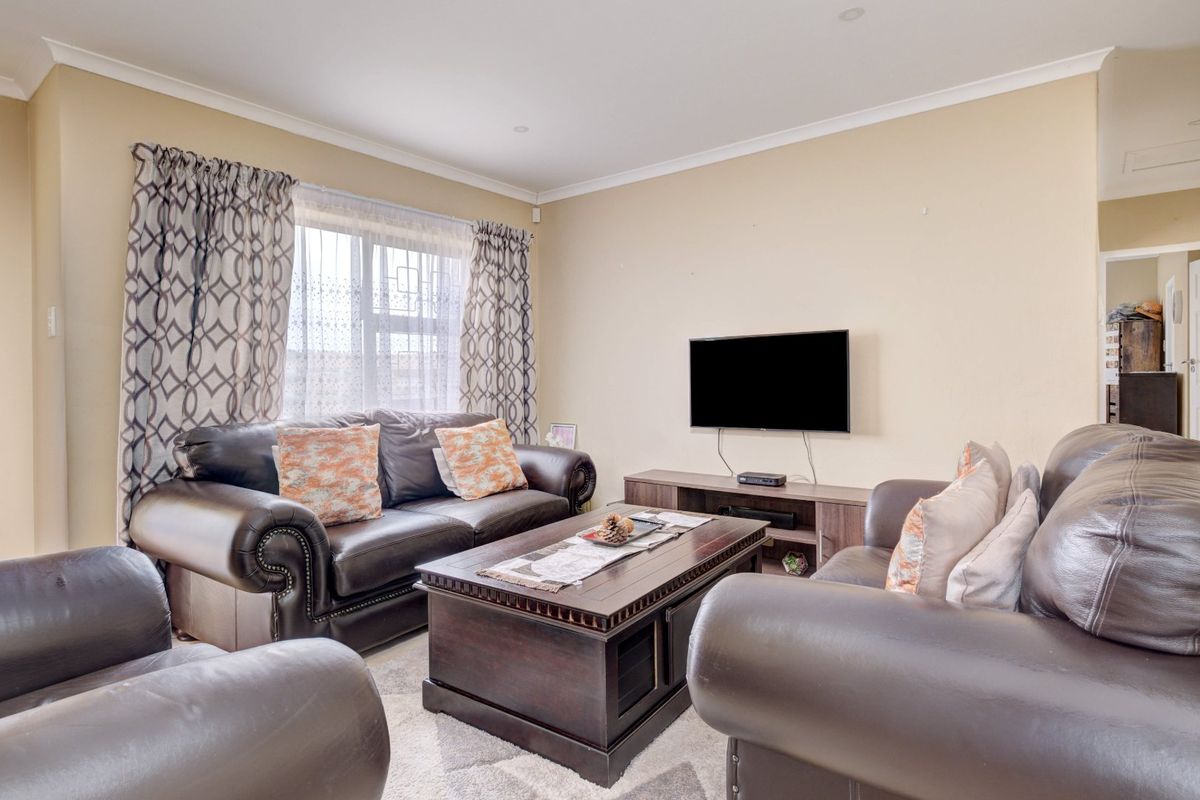 A comfortable living room featuring neutral wall tones, recessed downlighting, and a window fitted with security bars.