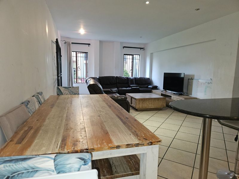 Spacious open-plan living and dining area featuring tiled flooring, recessed lighting, and large windows with security bars.