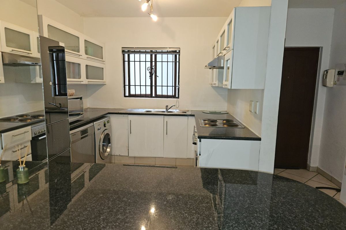 Functional kitchen featuring granite countertops, ample built-in cabinetry, integrated hob, and extractor fan, with a window fitted with security bars.