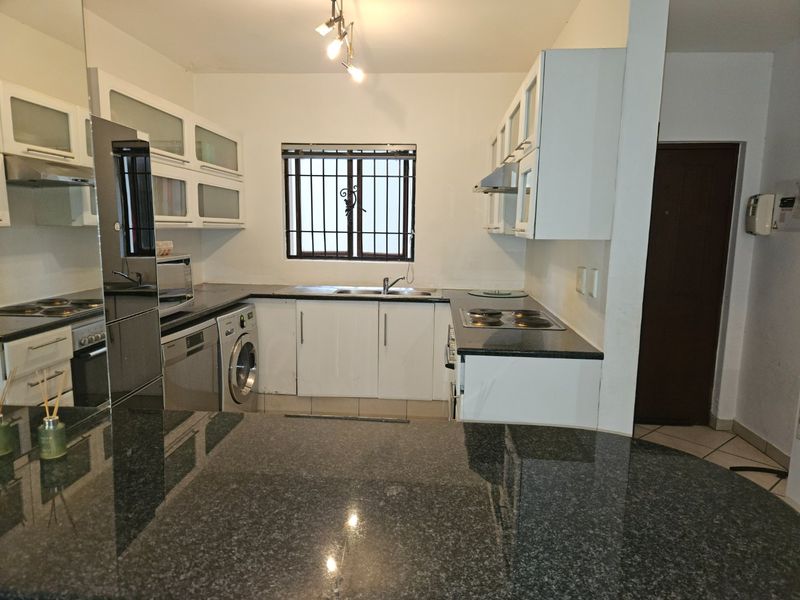 Functional kitchen featuring granite countertops, ample built-in cabinetry, integrated hob, and extractor fan, with a window fitted with security bars.