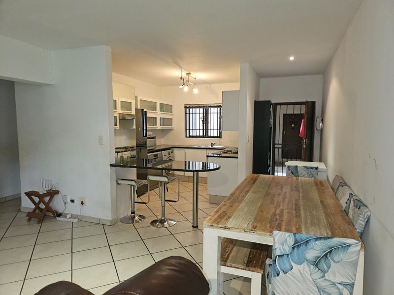 Open plan kitchen and dining area featuring tiled flooring, granite countertops, breakfast bar, and direct access to the entrance with security gate.