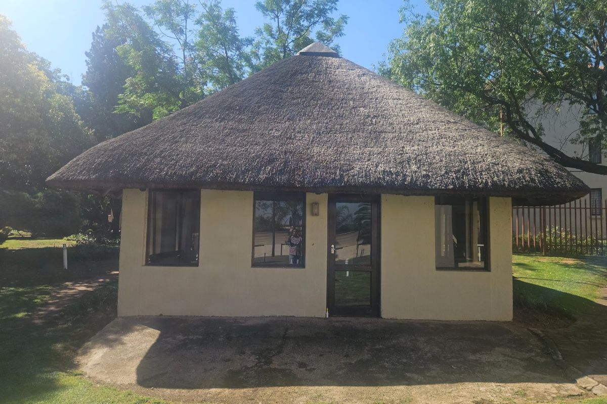 A detached garden structure featuring a traditional thatch roof, concrete patio area, and aluminium-framed windows set within a landscaped garden.