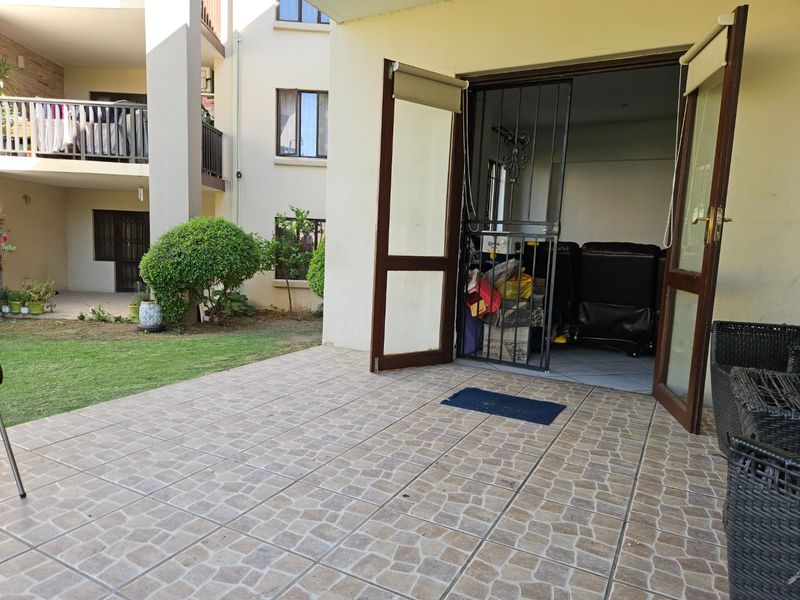 A ground floor tiled patio area featuring a security gate and double glass doors leading into the apartment living space.