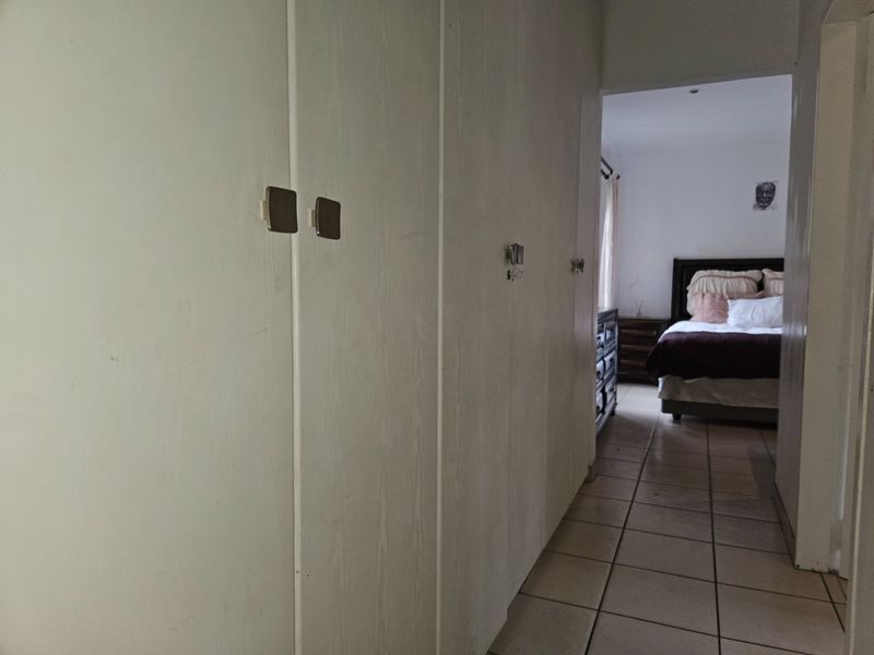 A hallway featuring built-in cupboards with tiled flooring, leading into a bedroom area.
