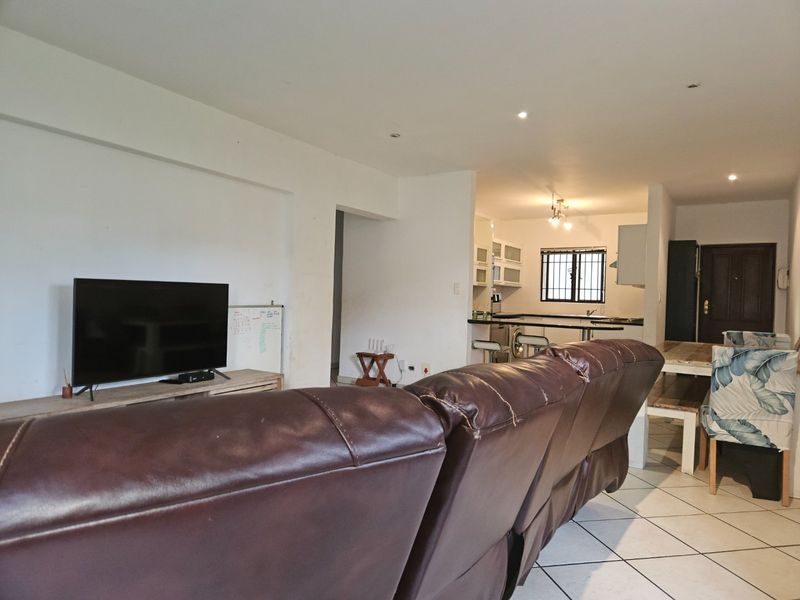 Open-plan living and kitchen area featuring tiled flooring, recessed lighting, and a functional kitchen layout with a breakfast bar.