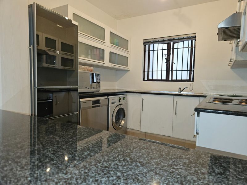 Functional kitchen featuring granite countertops, ample cabinetry, and integrated appliances, with a window providing natural light and security bars.