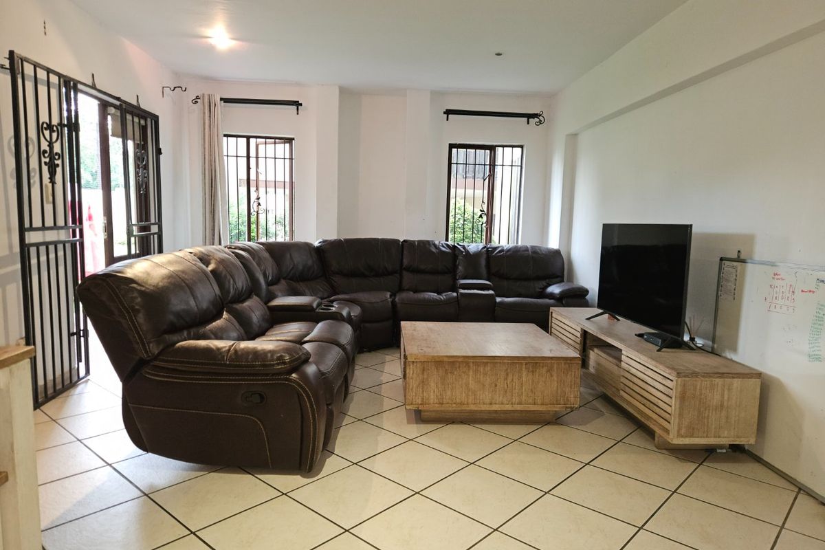 A spacious living room featuring tiled flooring, security gates on windows and doors, and recessed lighting, offering a functional layout for relaxation.