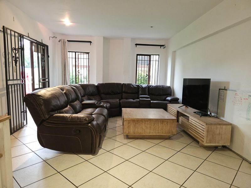 A spacious living room featuring tiled flooring, security gates on windows and doors, and recessed lighting, offering a functional layout for relaxation.