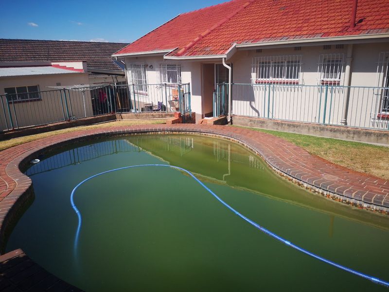 Rear exterior view featuring a swimming pool with brick coping and metal security fencing, adjacent to the main house structure.