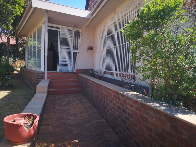 Front entrance area featuring a brick paved walkway, retaining wall, and covered patio with security gates and bars installed on windows.