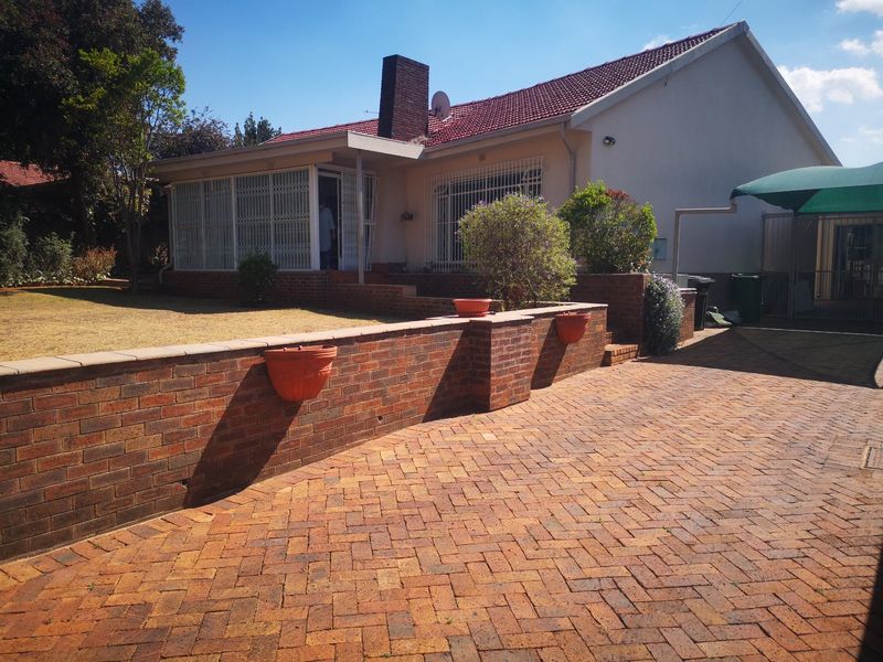 Front exterior view of a house featuring brick paving, a retaining wall, and a tiled roof with a prominent brick chimney.