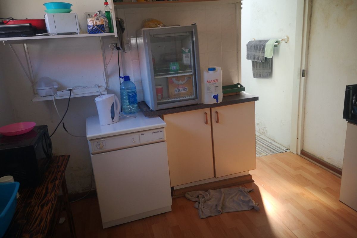A compact kitchen area featuring built-in cabinetry, laminate countertops, and wall-mounted shelving, requiring cosmetic updates to improve the overall condition.