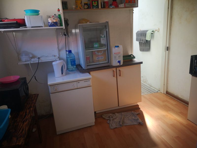 A compact kitchen area featuring built-in cabinetry, laminate countertops, and wall-mounted shelving, requiring cosmetic updates to improve the overall condition.