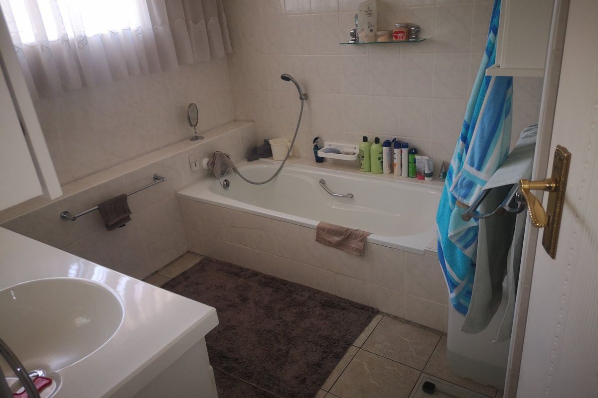 A functional bathroom featuring a built-in bathtub with handheld shower attachment, vanity basin, and neutral wall and floor tiling.