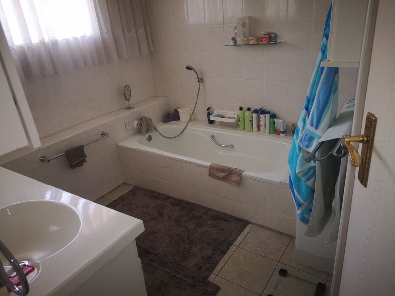 A functional bathroom featuring a built-in bathtub with handheld shower attachment, vanity basin, and neutral wall and floor tiling.