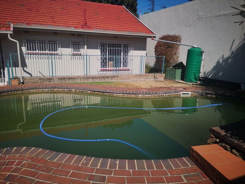Rear exterior view featuring a swimming pool with brick coping, a water storage tank, and security fencing against the house facade.