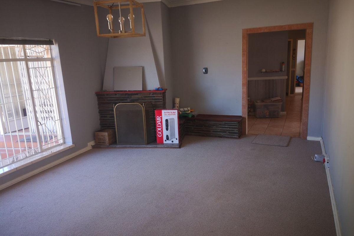 Spacious living room featuring a traditional stone fireplace, carpeted flooring, and large windows with security gates, offering a blank canvas for renovation.