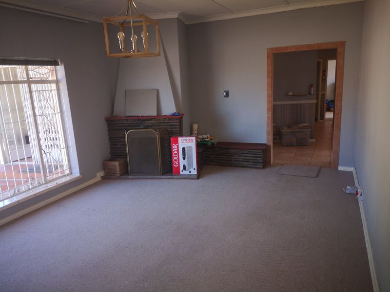 Spacious living room featuring a traditional stone fireplace, carpeted flooring, and large windows with security gates, offering a blank canvas for renovation.