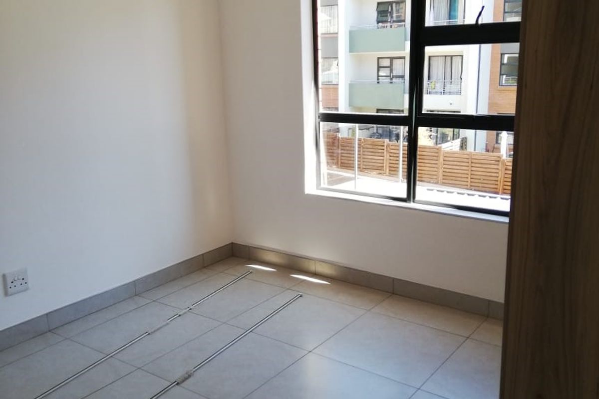 An empty bedroom featuring neutral tiled flooring, a large aluminium window, and a built-in cupboard, offering a clean and versatile living space.