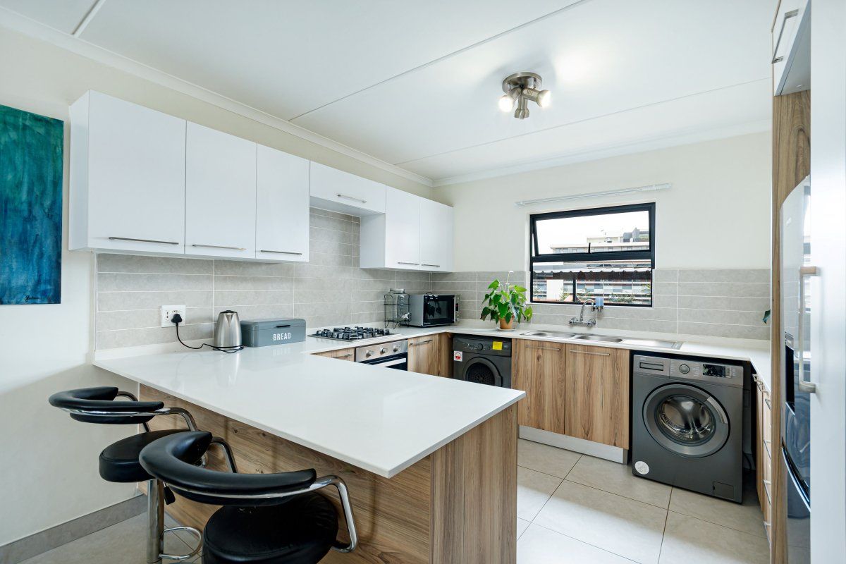 Modern kitchen featuring wood-grain and white cabinetry, stone countertops, gas hob, under-counter oven, and integrated laundry facilities with tiled flooring.