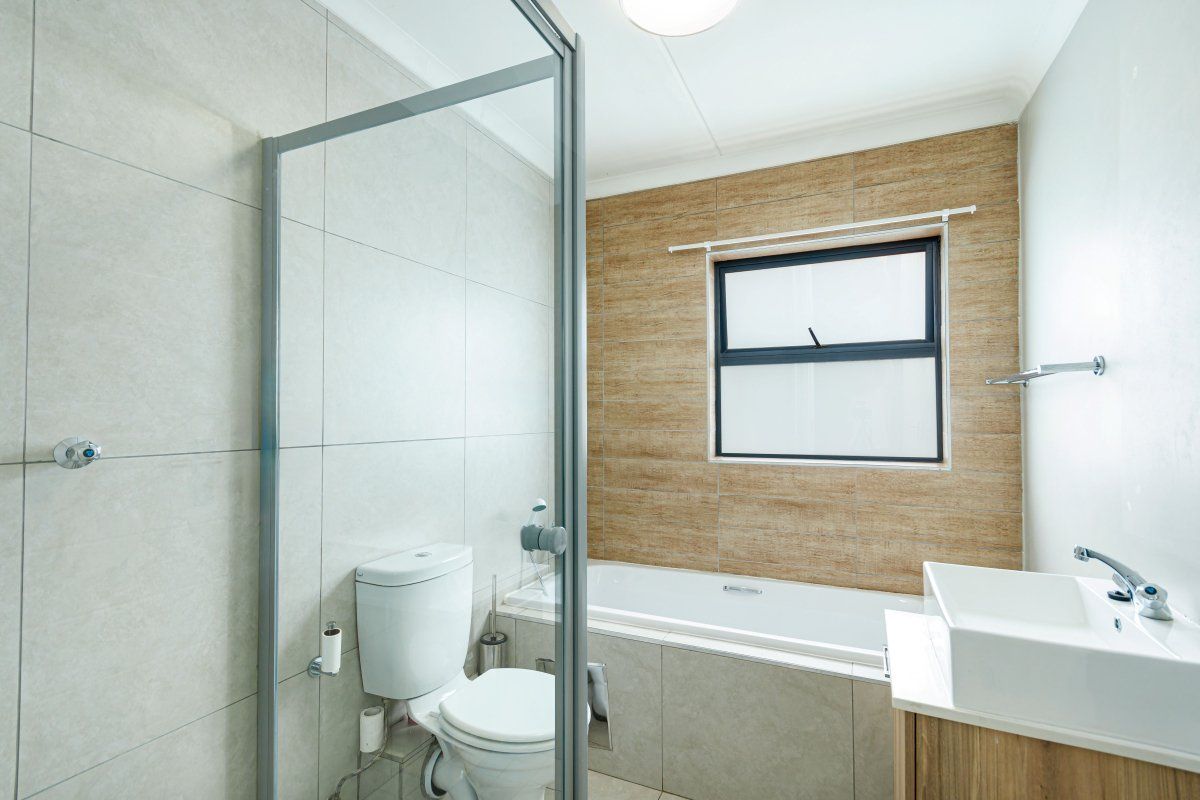 Modern bathroom featuring a glass shower enclosure, bathtub, vanity basin, and neutral tiled walls with a feature wood-look tile accent.