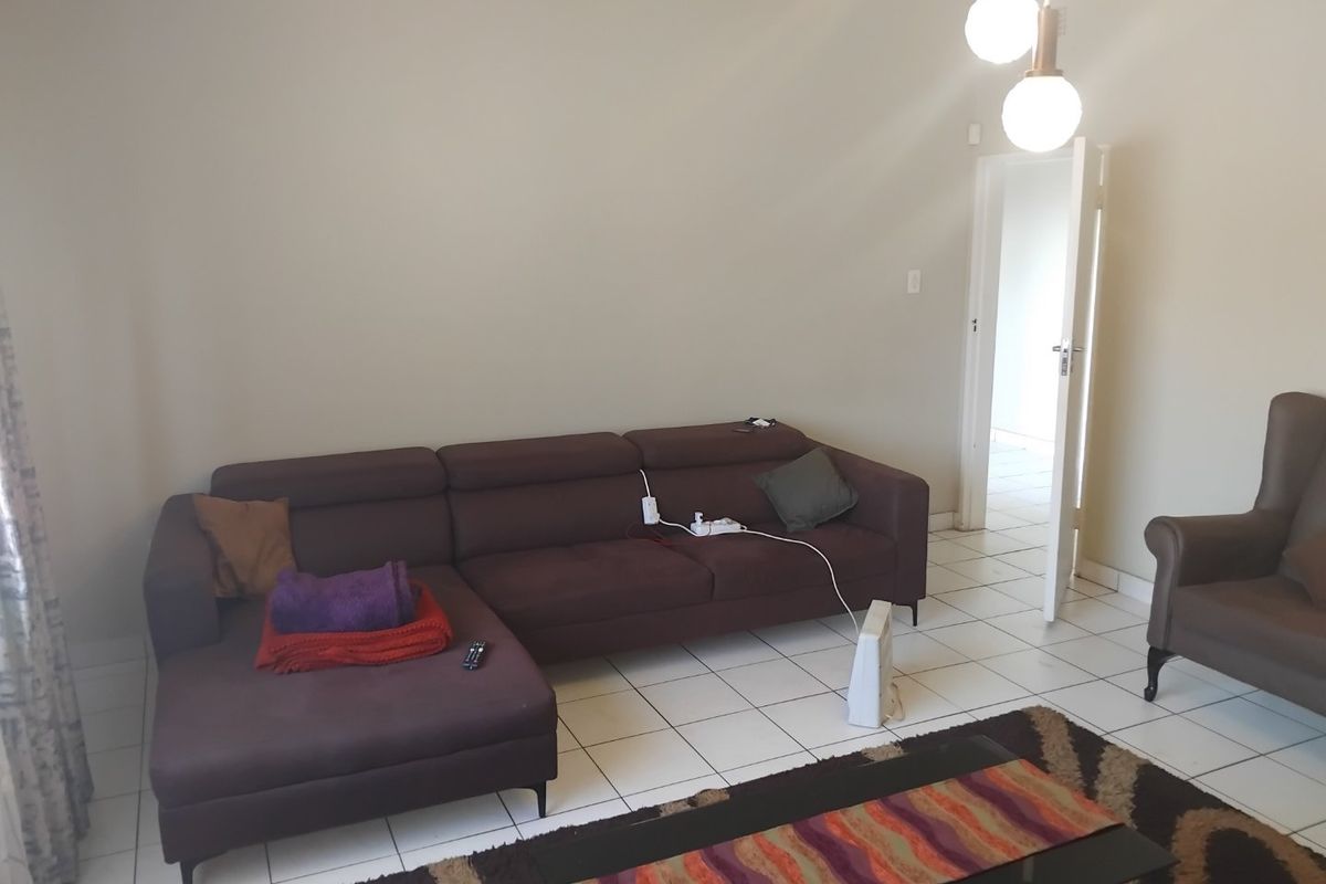 A living room featuring neutral wall tones, tiled flooring, and modern pendant lighting, providing a functional and open living space.