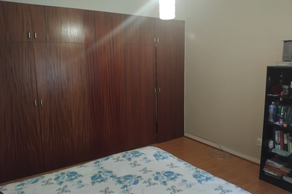 A bedroom featuring extensive floor-to-ceiling built-in wooden cupboards and laminate flooring, offering ample storage space.