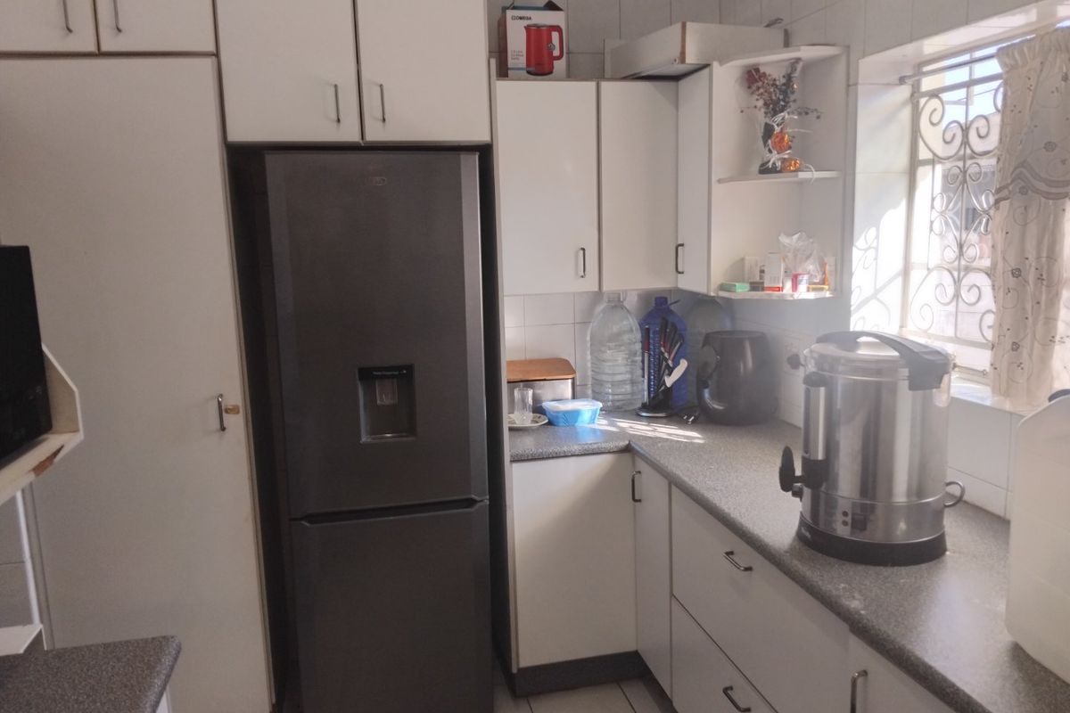 A functional kitchen featuring white built-in cabinetry, laminate countertops, tiled backsplash, and a window with security bars.