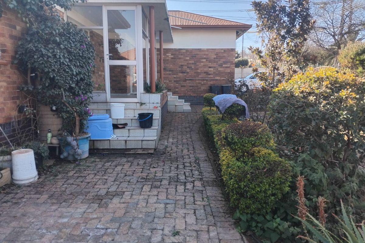 Rear exterior view featuring a brick-paved pathway, landscaped garden, and an enclosed patio area with tiled steps.