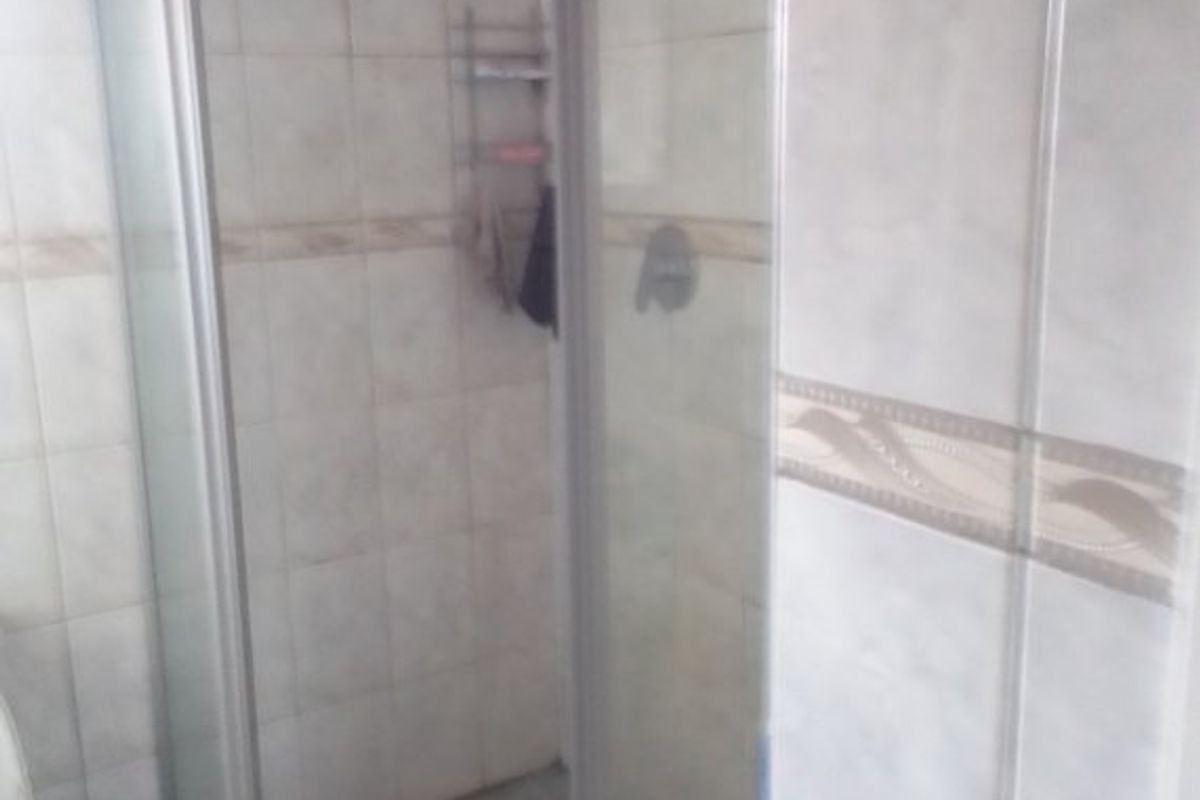 A dated bathroom featuring a corner shower enclosure with tiled walls and flooring, requiring cosmetic updates to improve the overall aesthetic.