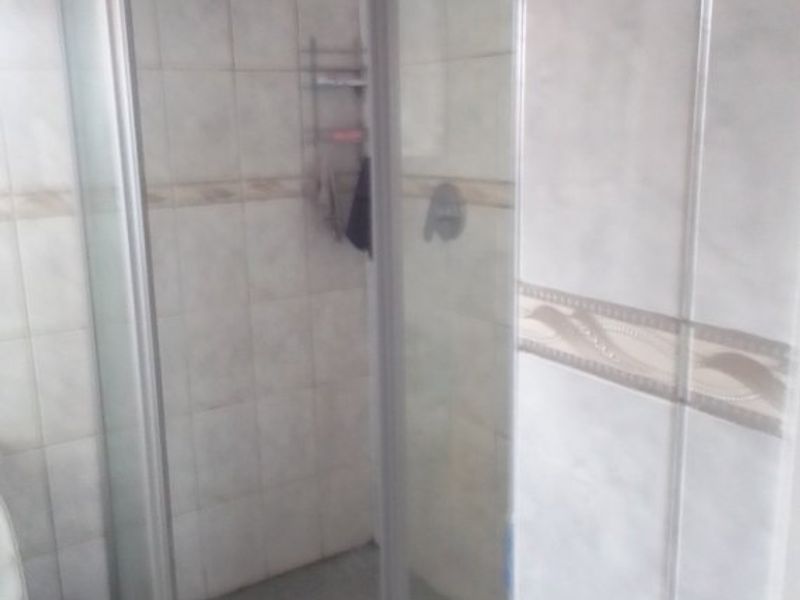 A dated bathroom featuring a corner shower enclosure with tiled walls and flooring, requiring cosmetic updates to improve the overall aesthetic.