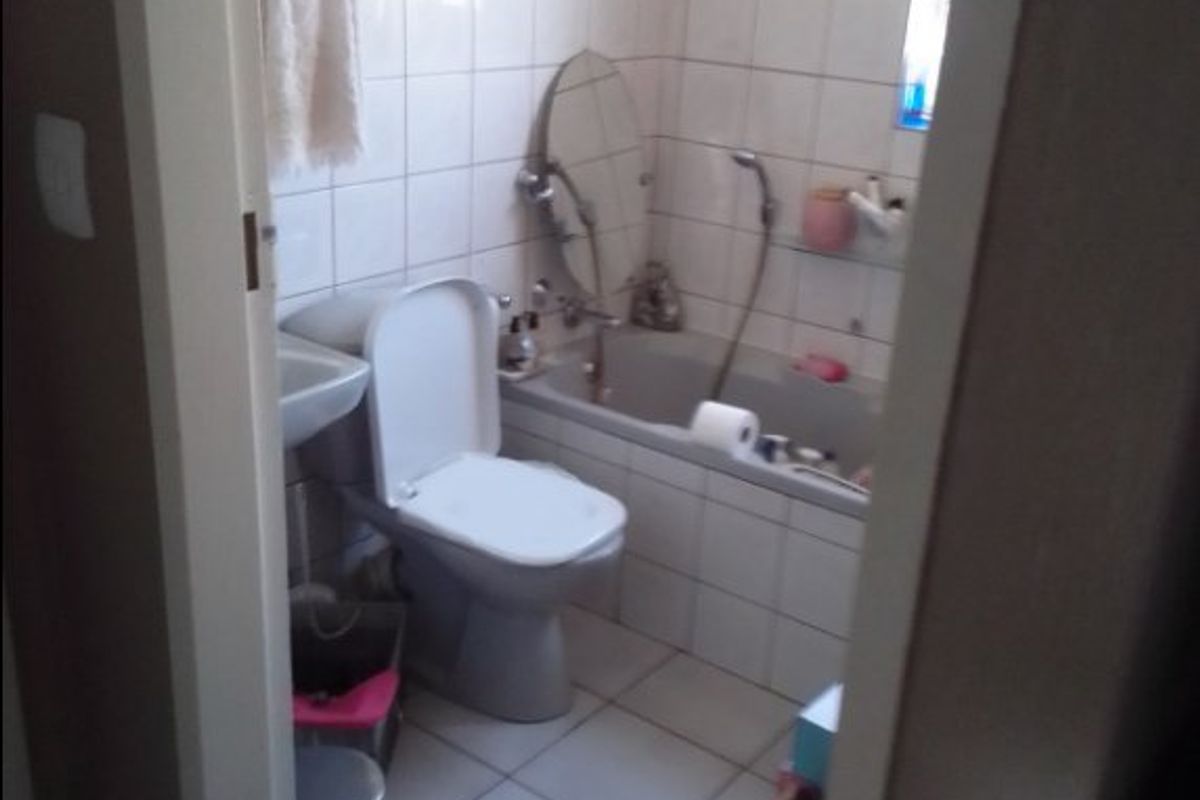 A functional bathroom featuring a bathtub, toilet, and wall-mounted basin with tiled finishes throughout.