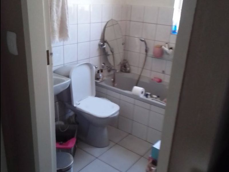 A functional bathroom featuring a bathtub, toilet, and wall-mounted basin with tiled finishes throughout.