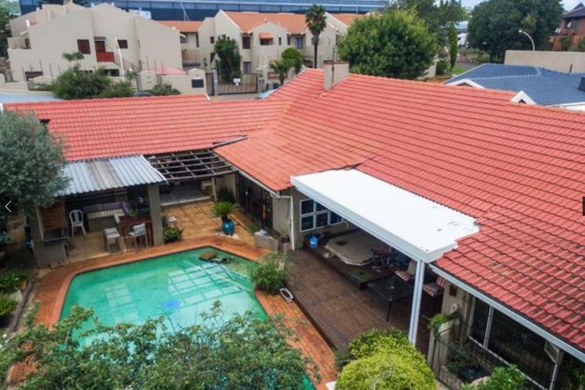 Aerial view of the rear property featuring a swimming pool, covered patio area, and timber decking under a terracotta tiled roof.