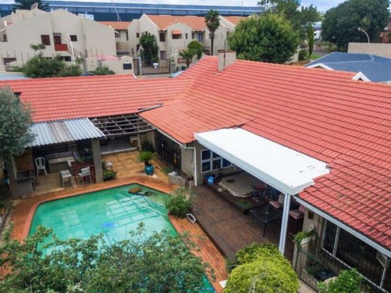 Aerial view of the rear property featuring a swimming pool, covered patio area, and timber decking under a terracotta tiled roof.