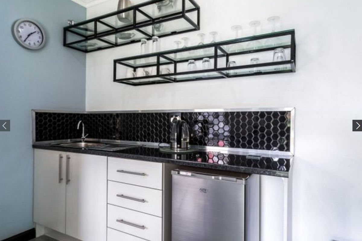 Compact kitchenette featuring modern white cabinetry, black granite countertops, a striking hexagonal tile backsplash, and stylish industrial-style wall-mounted glass shelving.