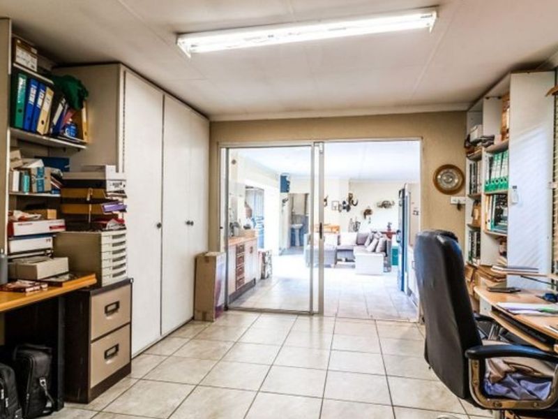 A functional home office space featuring built-in storage cabinetry, tiled flooring, and sliding glass doors providing access to the adjacent living area.