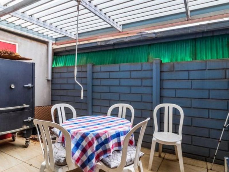 Covered patio area featuring a metal pergola structure and a solid masonry boundary wall, providing a functional outdoor entertainment space.