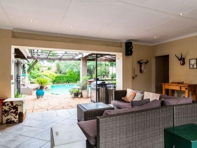 Spacious covered patio area featuring tiled flooring and recessed lighting, seamlessly flowing out to a private swimming pool and garden space.