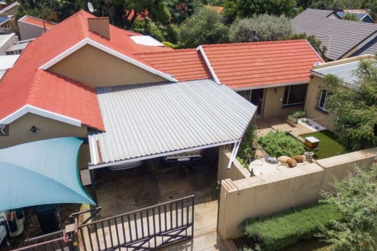 Aerial view of the property featuring a tiled roof, a corrugated metal carport, a paved driveway, and a small landscaped garden area.