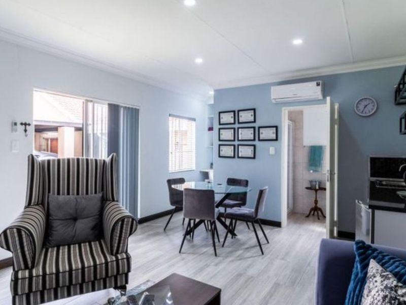 Open-plan living and dining area featuring light wood-look flooring, recessed ceiling lighting, and a wall-mounted air conditioning unit.