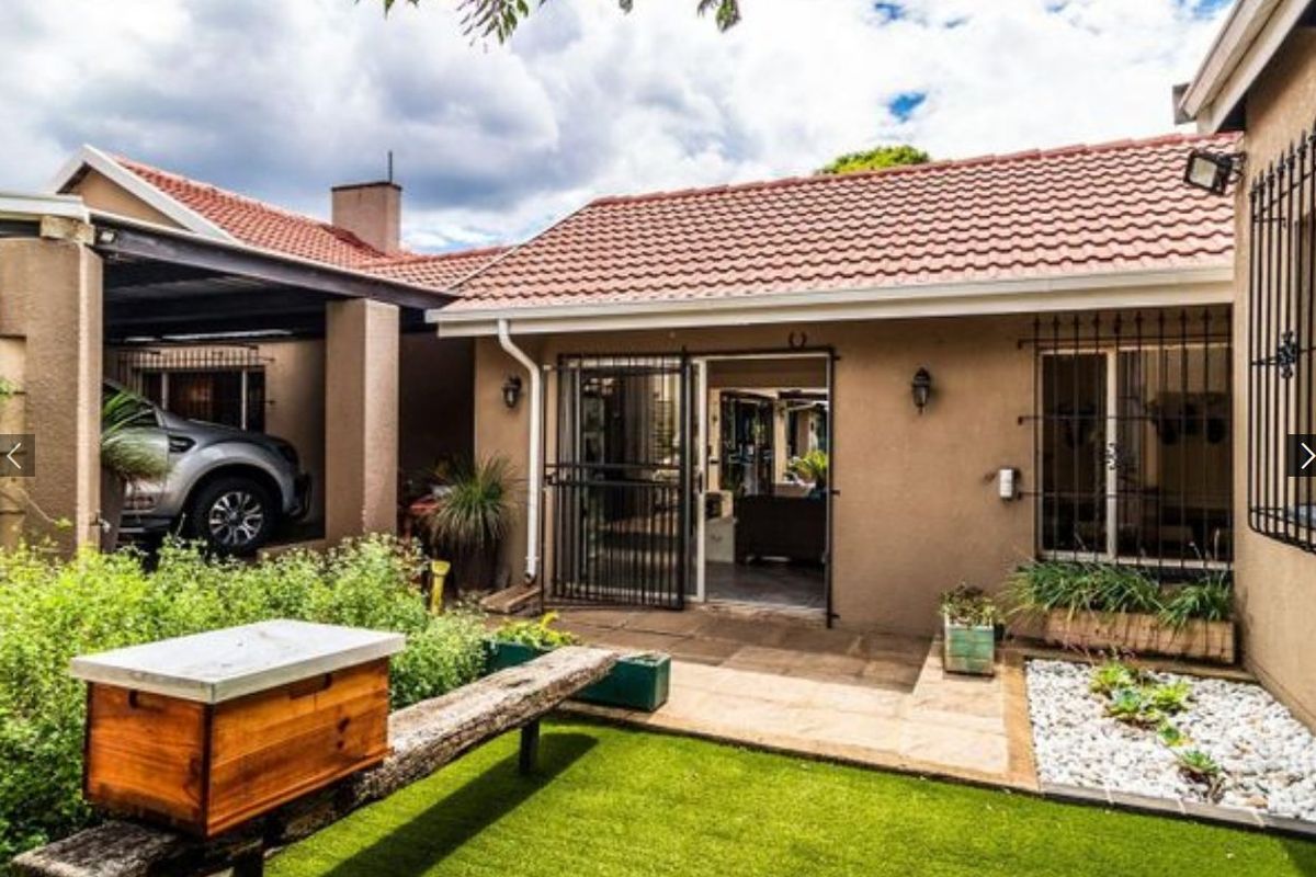 Rear exterior view of the house featuring a tiled roof, paved patio area, security gates, and a small garden space with artificial lawn.