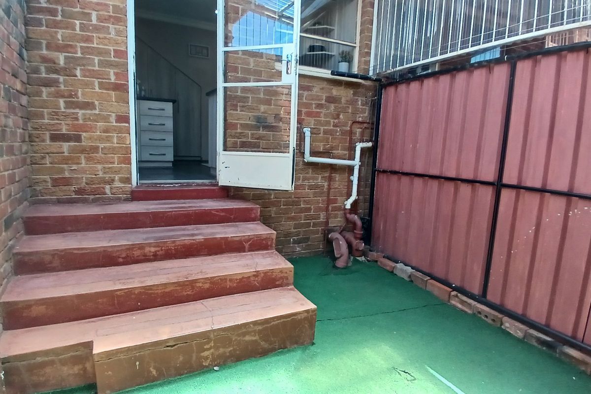 Rear exterior area featuring brick walls, concrete steps leading to the entrance, and corrugated metal fencing.