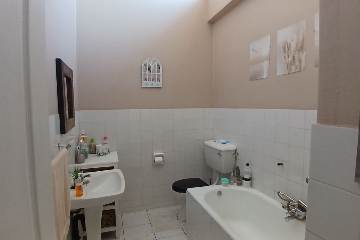 A functional bathroom featuring a pedestal washbasin, standard toilet, and a bathtub with partial wall tiling.