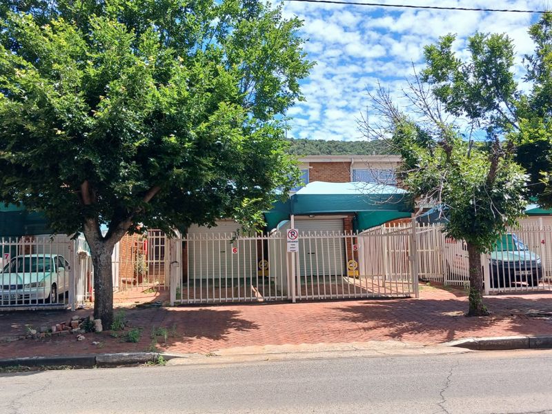 Front view of a townhouse complex featuring brick paved driveway, secure metal fencing, and covered carport parking bays.