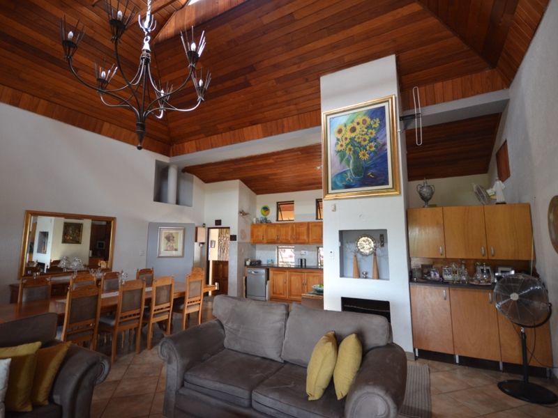 Spacious open-plan living and dining area featuring a high vaulted timber ceiling, tiled floors, a central fireplace, and integrated kitchen cabinetry.